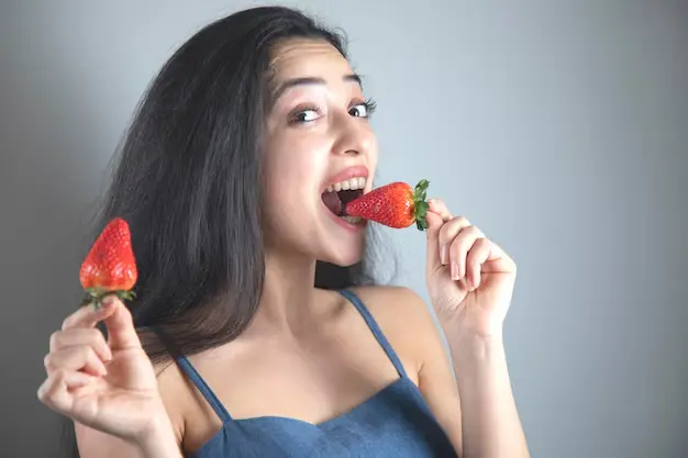 امرأة تأكل فراولة لتساعدها طبيعيا على تبييض الأسنان