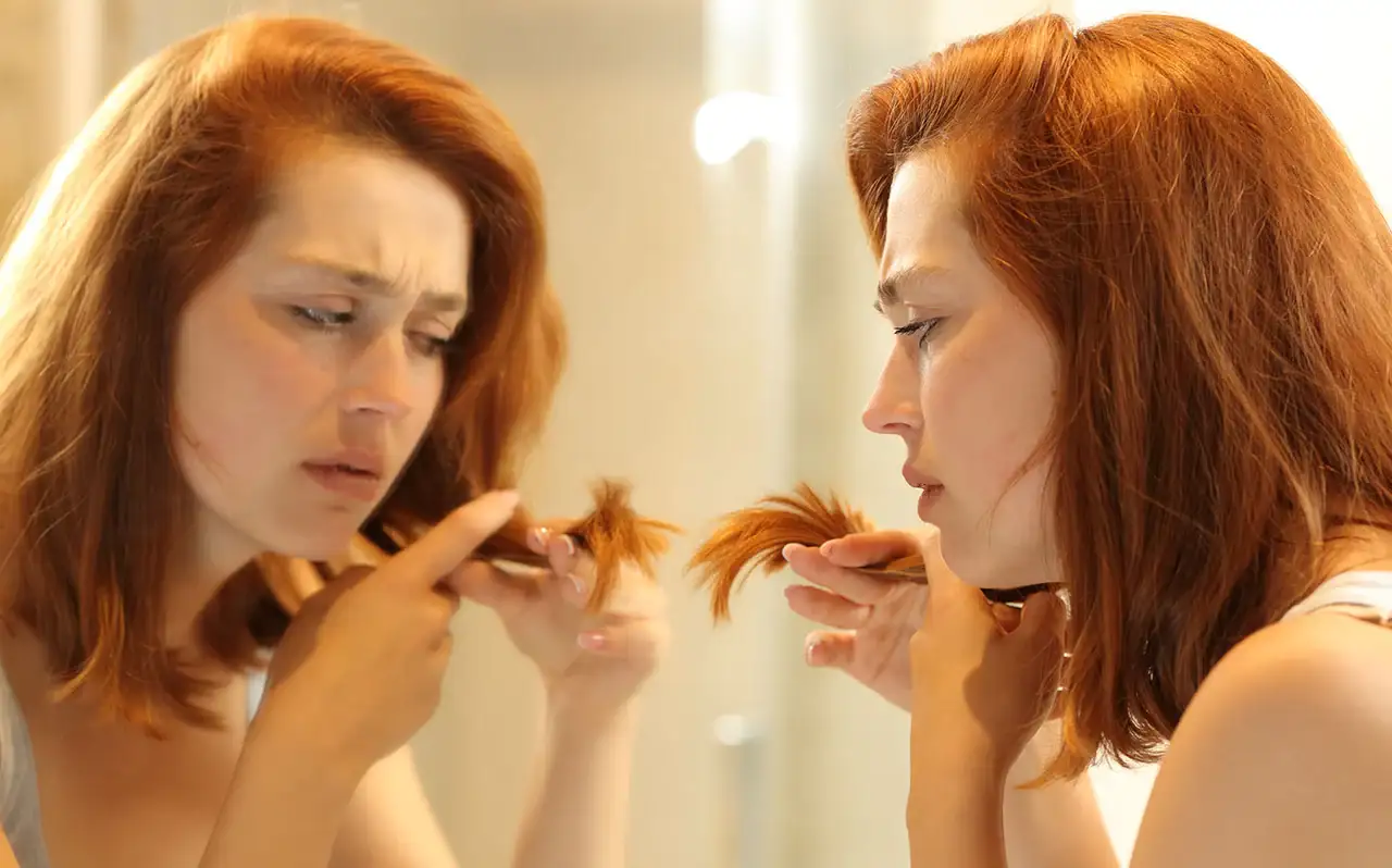 امرأة تنظر في المرآة لشعرها التالف المتقصف